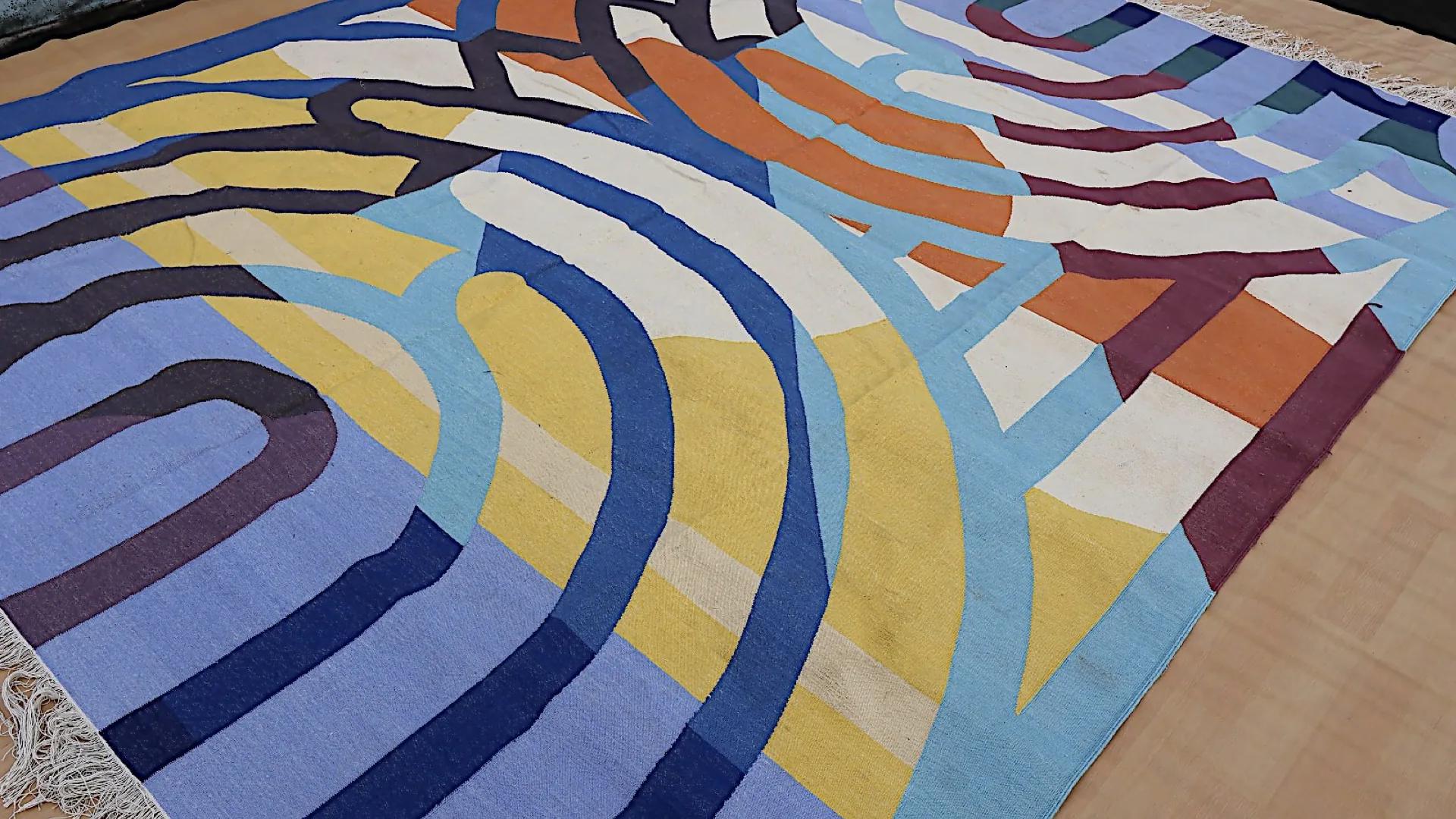 A finished hand-woven dhurrie at an angle, wool weave and fringed edge in a bold contemporary abstract pattern.