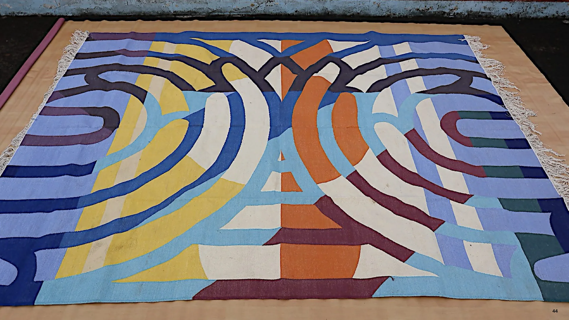 A finished Dadar Edit dhurrie laid flat, a bold abstract weave in blue, yellow, orange, and white.