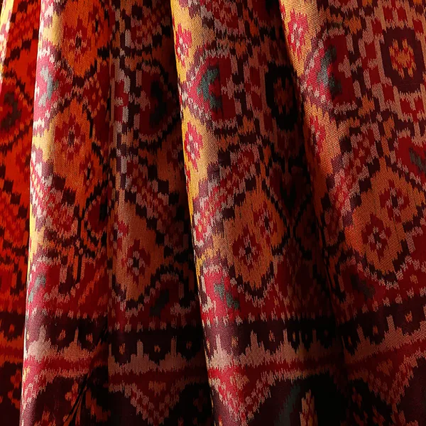 A draped Patan Patola double-ikat silk in red, maroon, and gold with geometric medallion patterning.